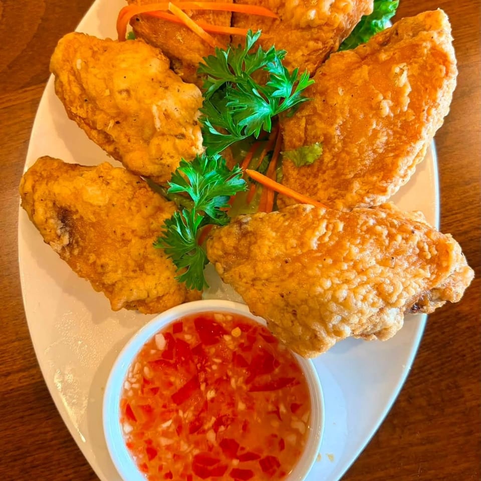 Crispy fried chicken wings with fresh parsley, carrot strips, and a side of chili dipping sauce.