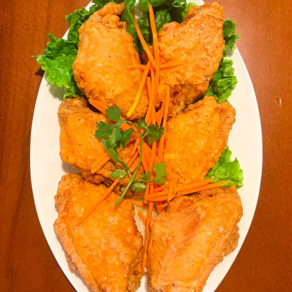 A white oval plate holds five golden-brown fried chicken wings, garnished with lettuce, shredded carrots, and cilantro.