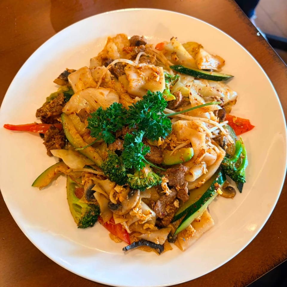 A close-up of a colorful stir-fry dish with noodles, beef, and various vegetables on a white plate.