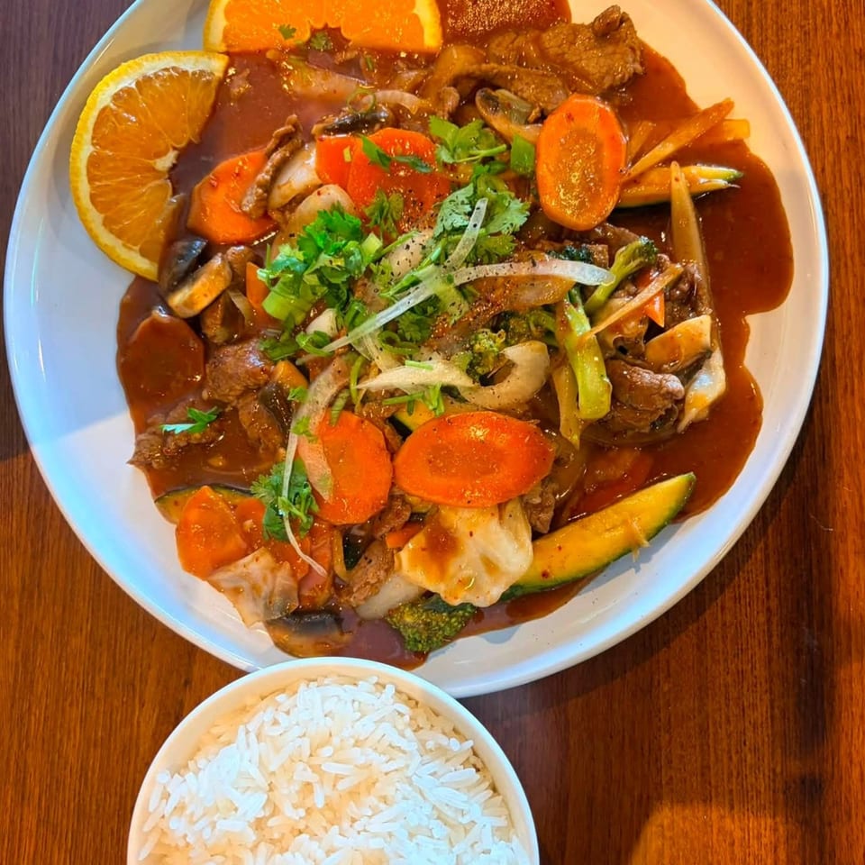 Beef stir-fry with vegetables and orange slices, served with a side of white rice.